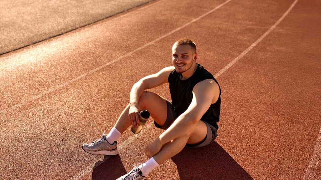 Young man holding a sports bottle sitting on a professional running track